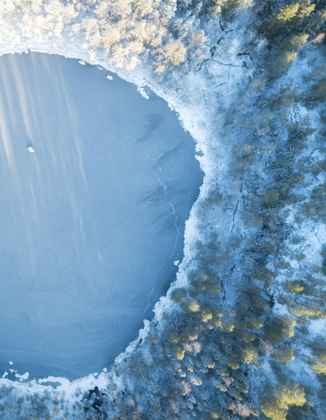 Аerial view of snow covered forest around beautiful lake. Rime ice and hoar frost covering trees. Scenic winter landscape near Helsinki, Finland.