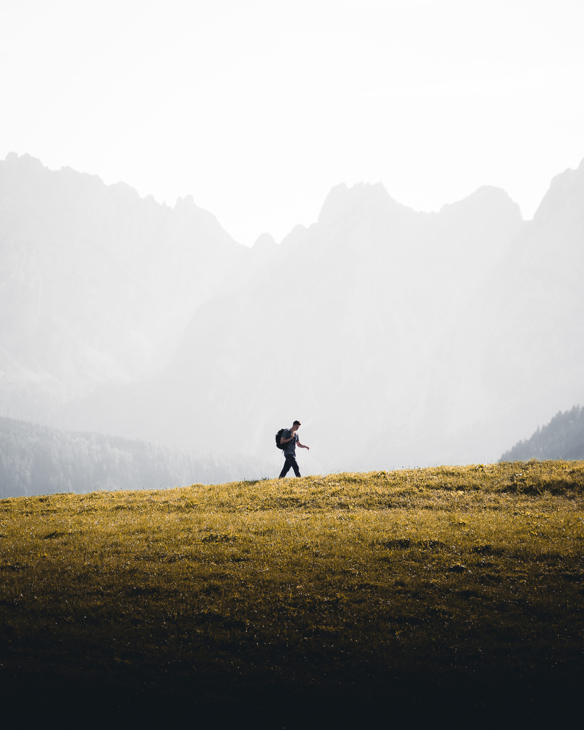 Lone male hiker walking on a grassy hill against a misty mountain landscape